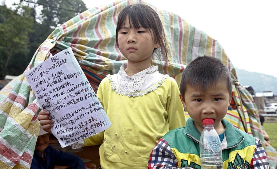 雅安“小英雄”的地震日記  4月21日，四川雅安地震重災區蘆山龍門鄉，在一個農田裡的自制簡易“抗震棚”外，9歲的姐姐高夢思正在展示她在20日地震時救出身旁弟弟后寫的日記。中新社發 張浩 攝